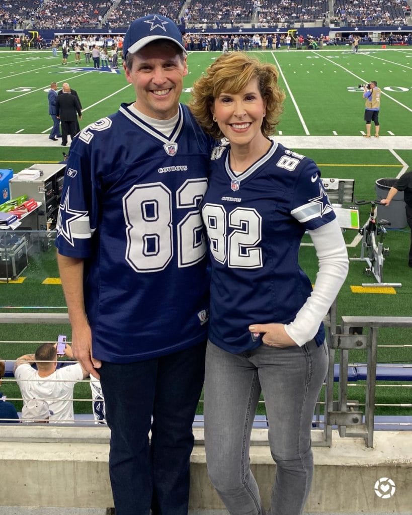 couple dressed in dallas cowboys jerseys standing on the sideline of a dallas cowboys game