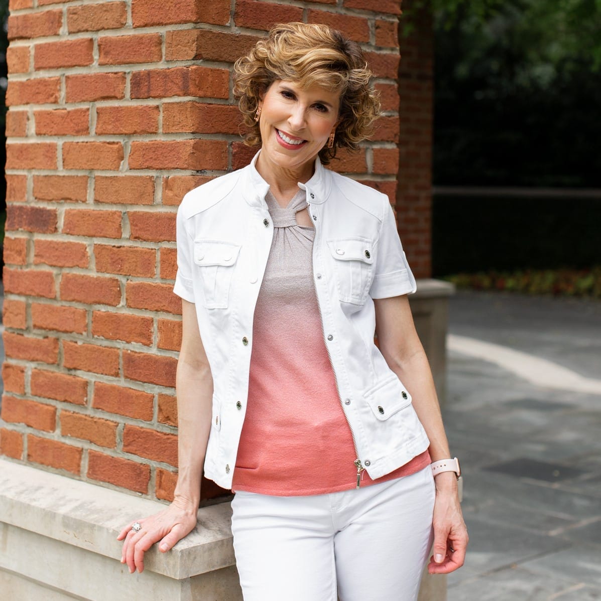 woman leaning against brick pillar wearing ombre top and white short sleeve jacket