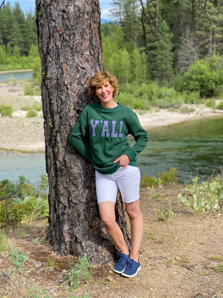 woman wearing marley lilly y'all sweatshirt posing by a pine tree