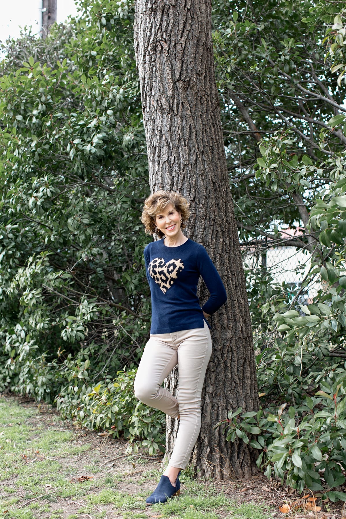 woman in heart sweater leaning against a tree