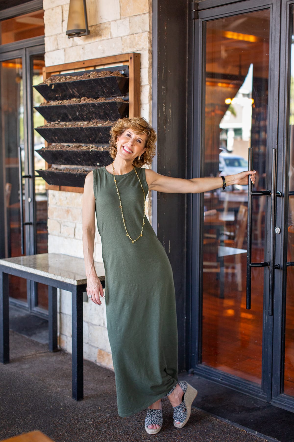 woman in green maxi dress standing at a door on a restaurant patio