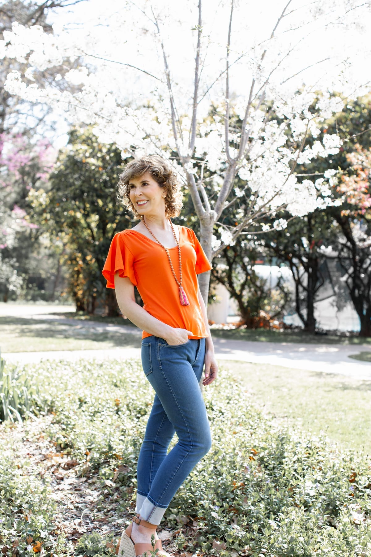 woman in orange shirt and tassel necklace in park