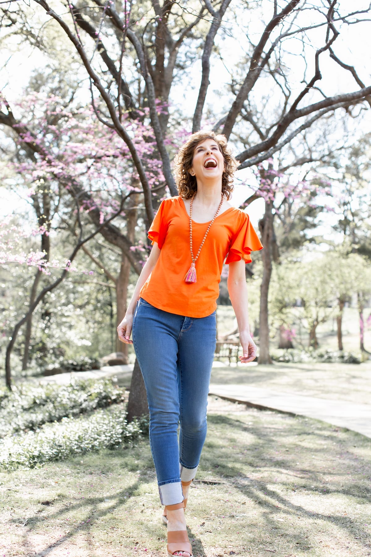 woman in orange shirt and tassel necklace in park