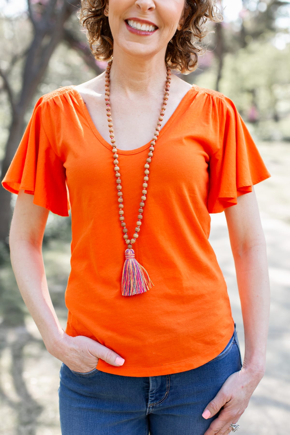 woman in orange shirt and tassel necklace in park