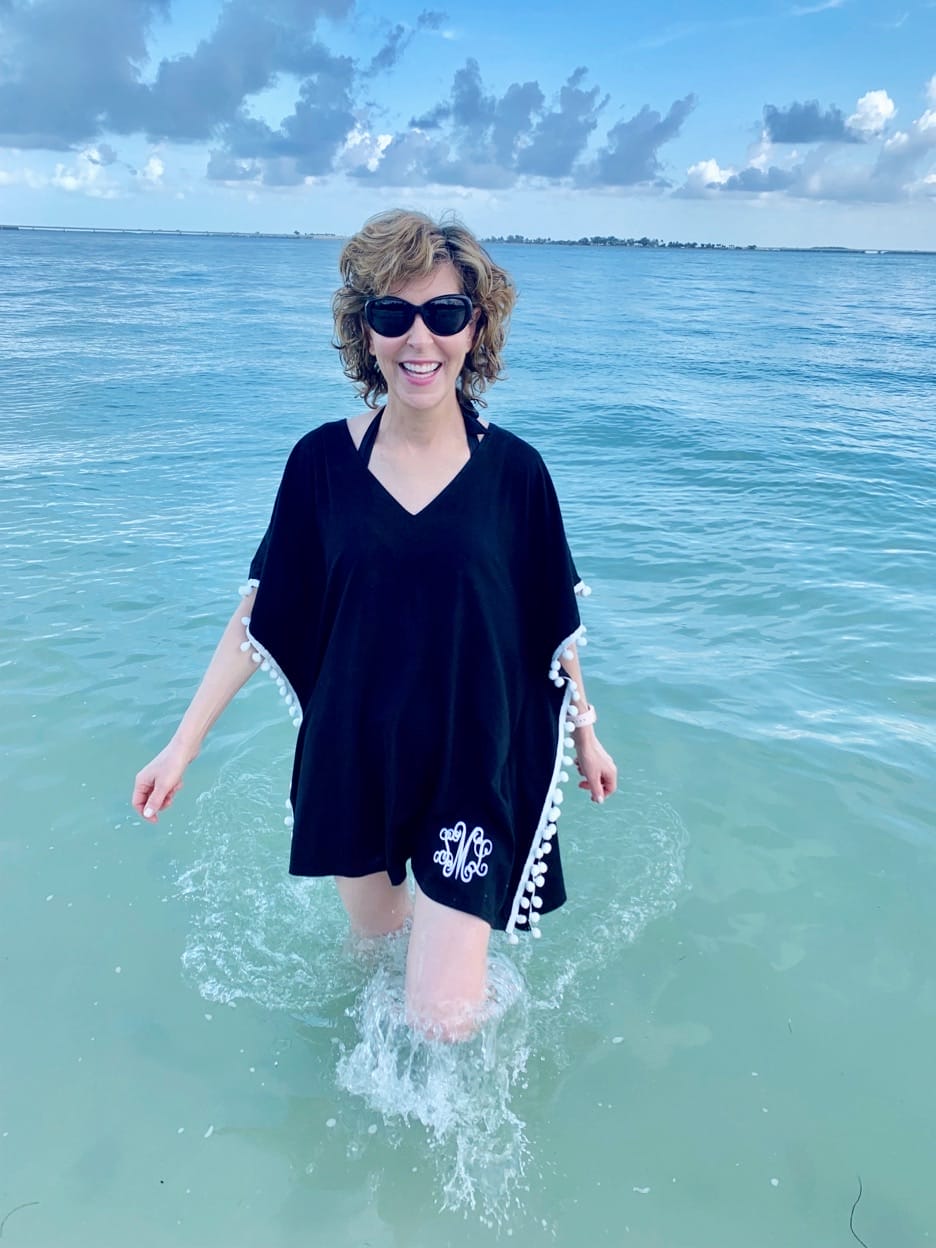 woman walking in shallow water on the beach in sanibel island wearing black coverup and sunglasses