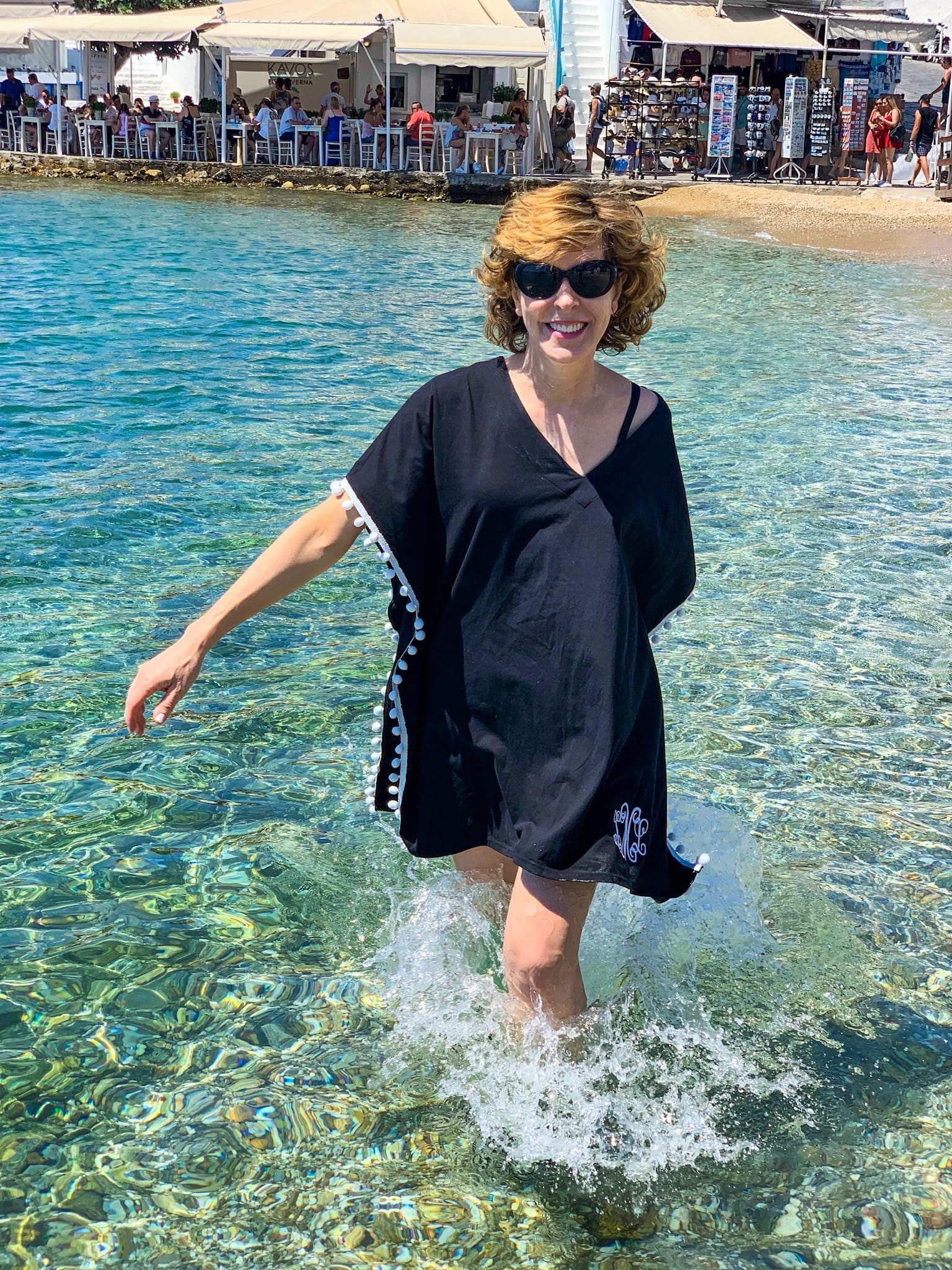 a woman wearing a black coverup in the water in mykonos greece