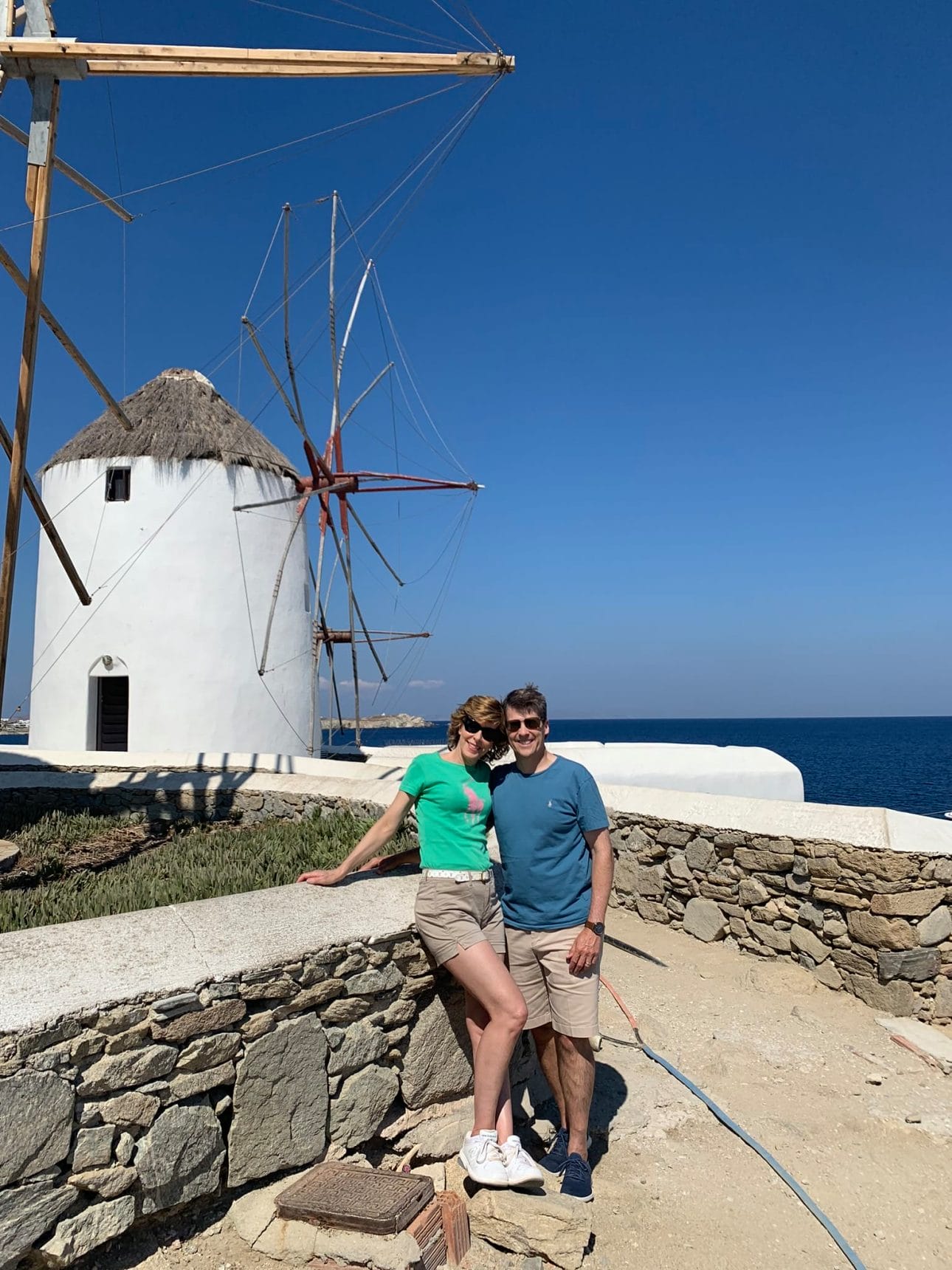 couple standing in front of windmills in mykonos greece