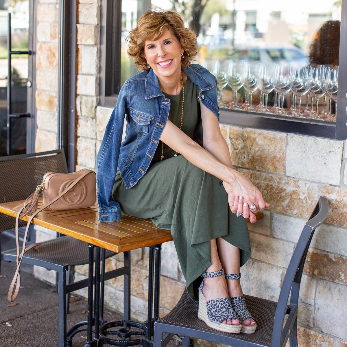 woman in green dress and denim jacket sitting on a restaurant patio table