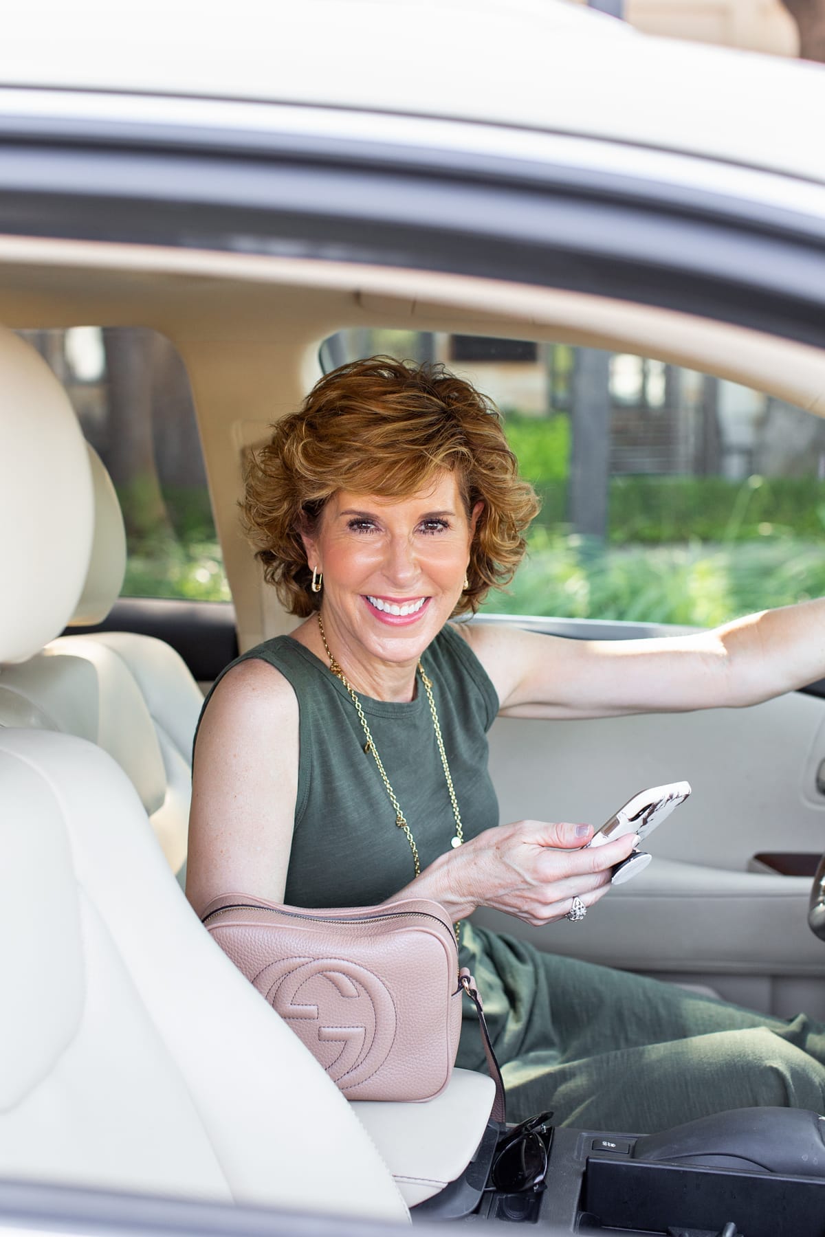 woman in green dress sitting in her car holding her phone looking at camera