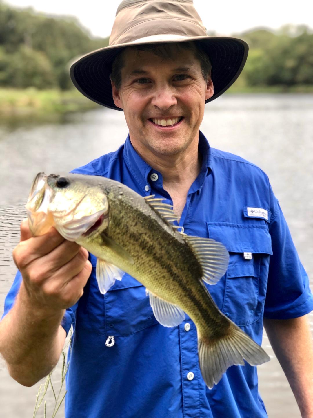 man in hat and blue shirt holding a bass caught at long cove