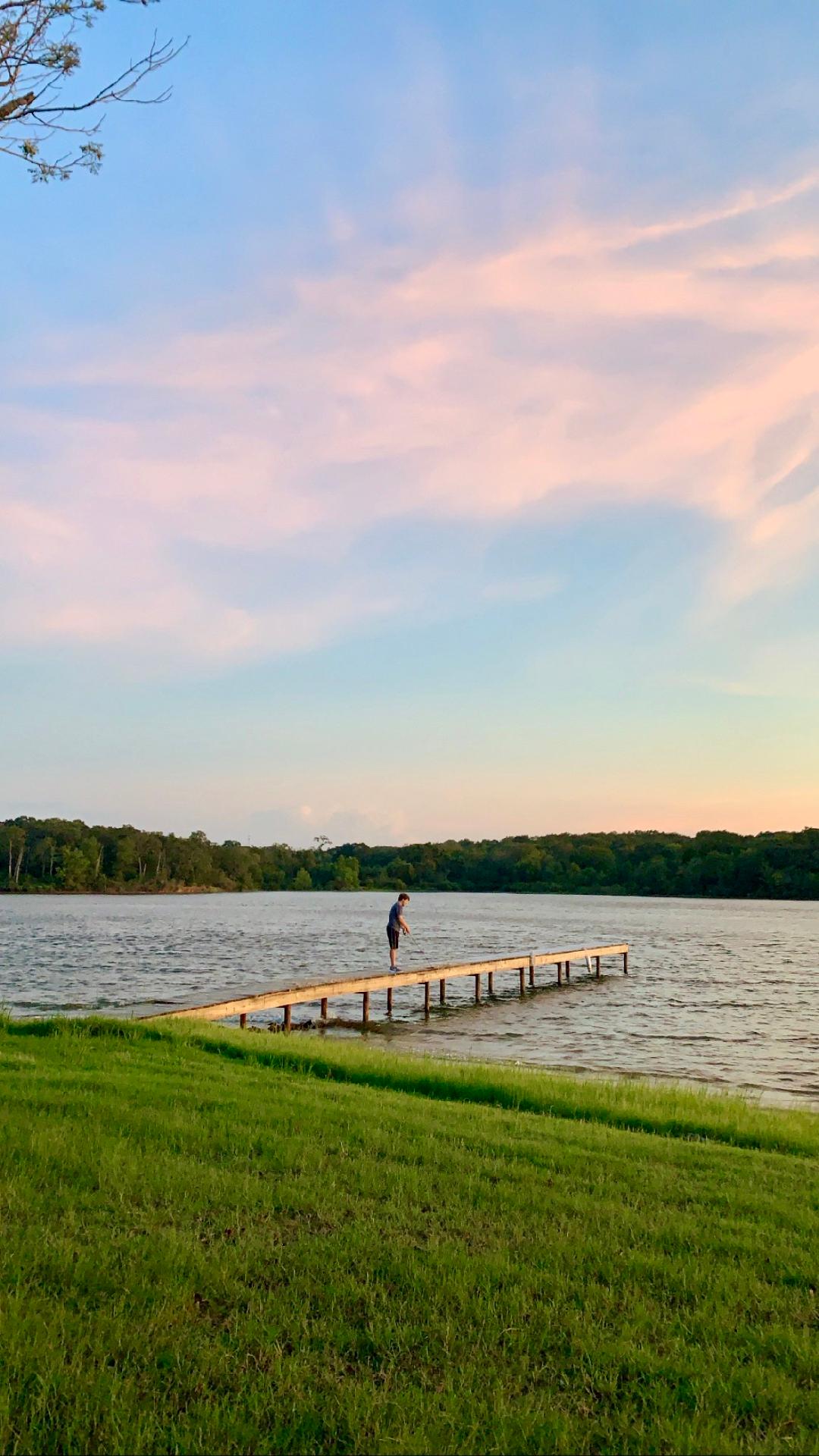 man fishing on a dock at sunset at long cove