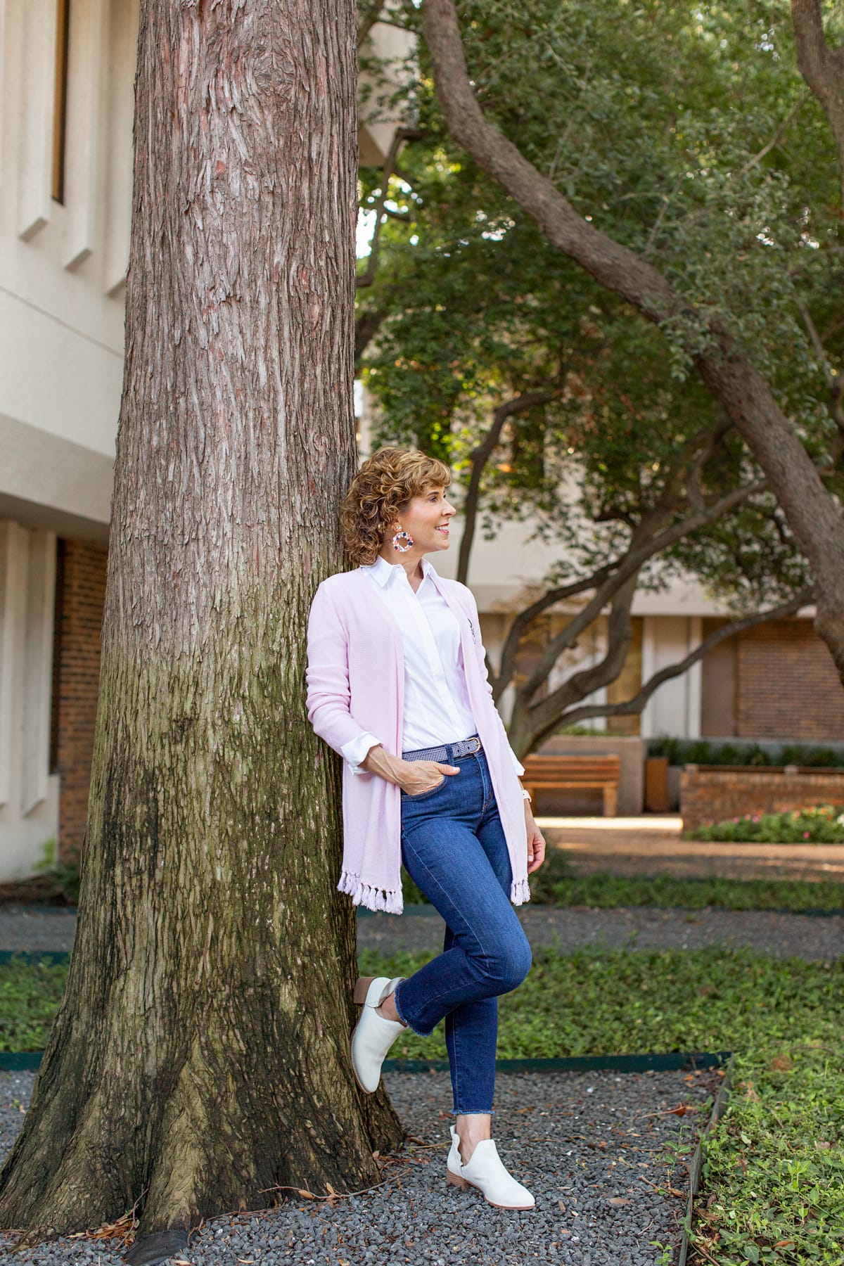 woman in pink cardigan standing next to a tree trunk looking to the side