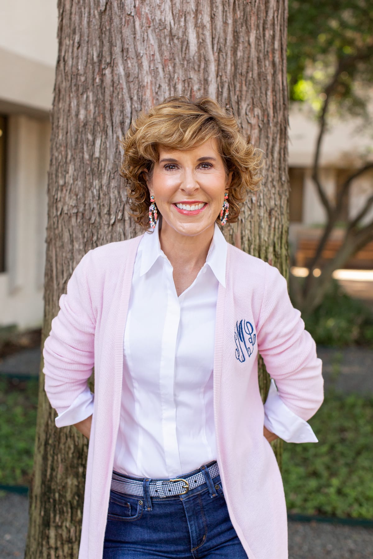 woman in pink cardigan standing next to a tree trunk looking at the camera