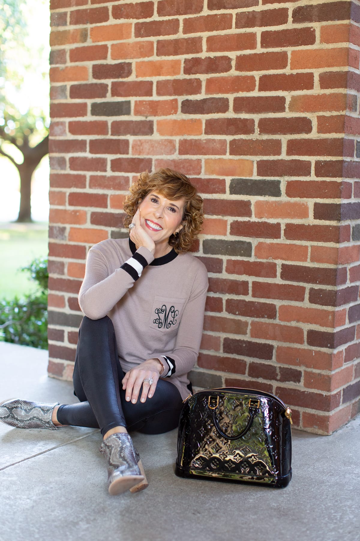 woman in tan monogrammed sweater sitting in front of a brick wall