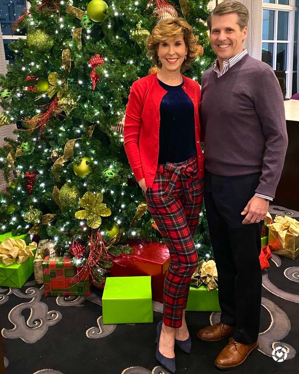 couple in holiday party attire standing in front of a christmas tree