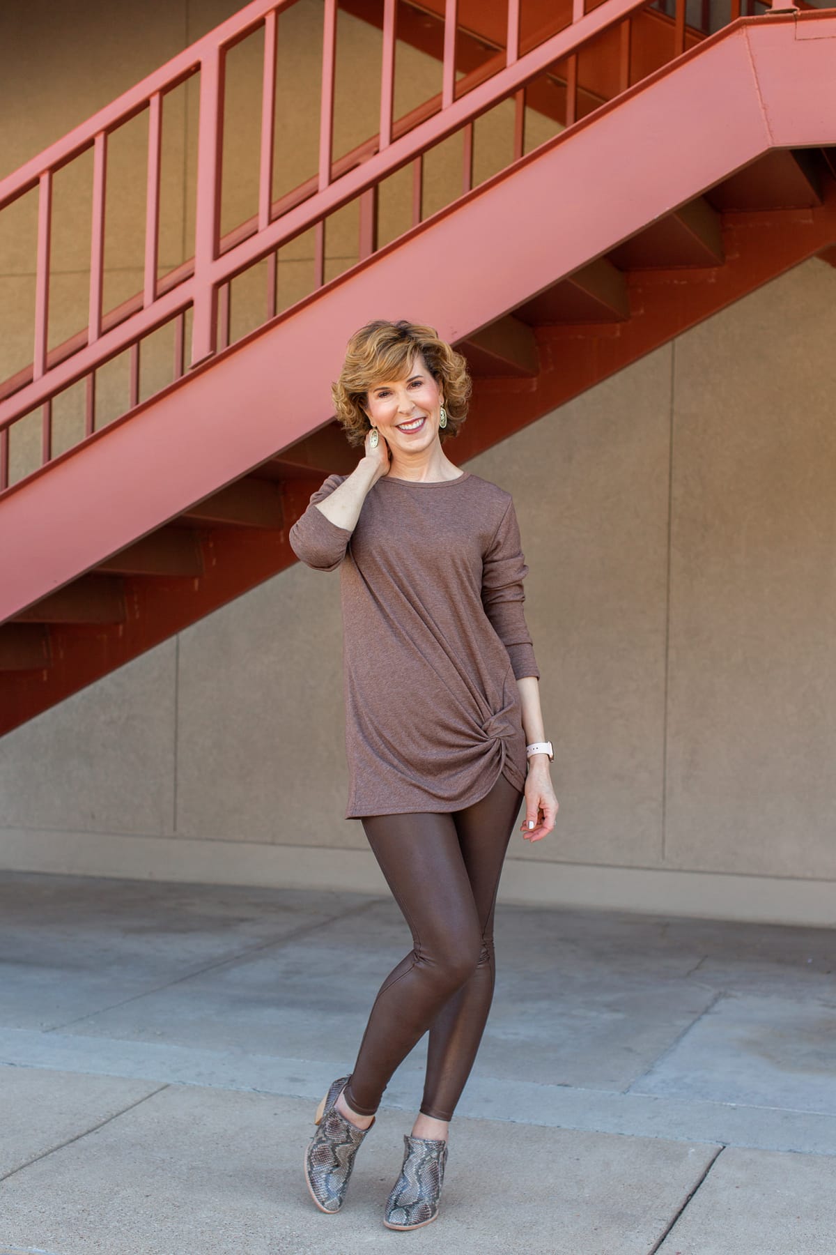 woman dressed in brown standing in front of a rust colored staircase