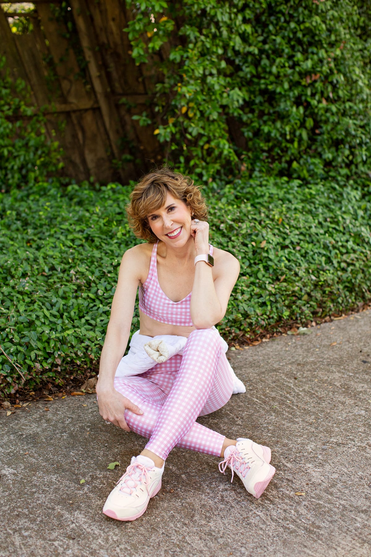 woman siting on the ground wearing pink and white workout wear and tennis shoes