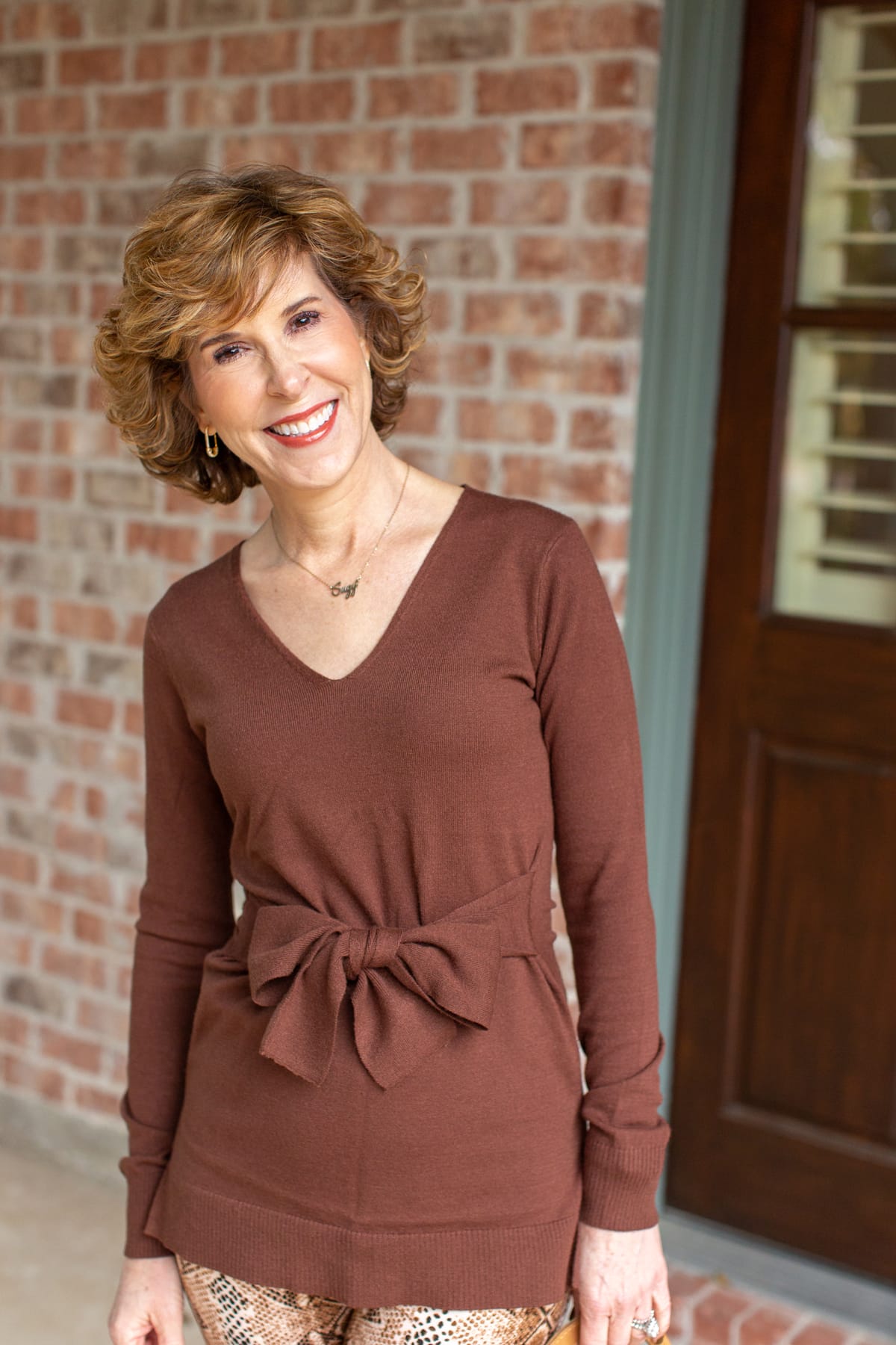 woman in brown tie waist sweater outside a house