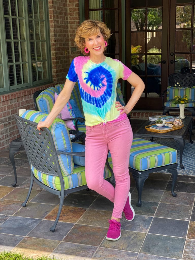 woman over 50 wearing tie die tee and pink jeans on a patio