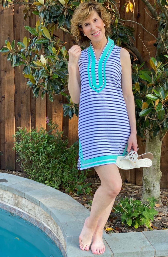 woman in blue stripe tunic dress with green trim standing by the side of a pool