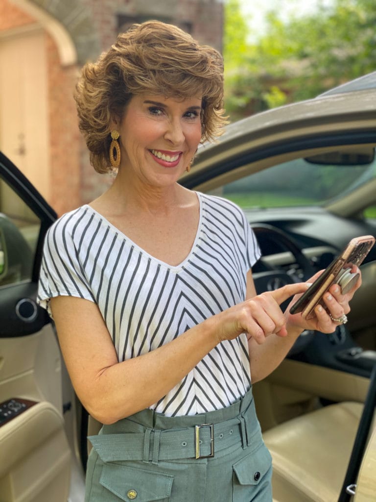 woman in green striped shirt standing by car looking at cell phone