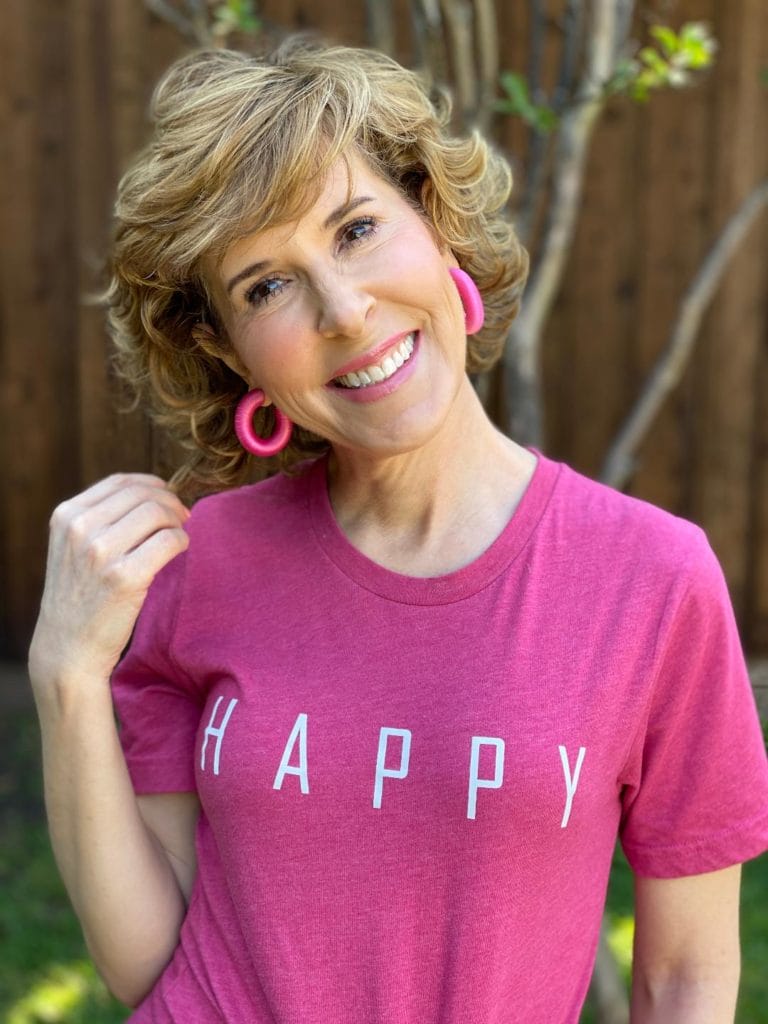 woman with hair over 50 wearing a happy tee and touching her hair