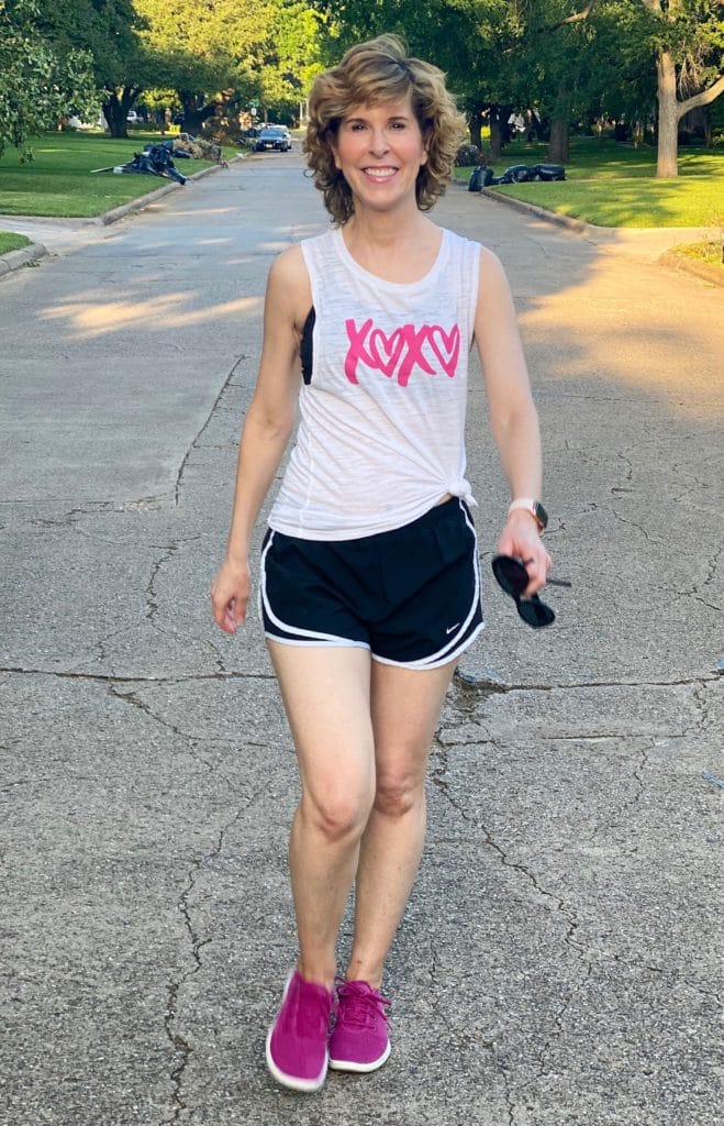 woman wearing xoxo tank top and black shorts and walking down the middle of a residential street