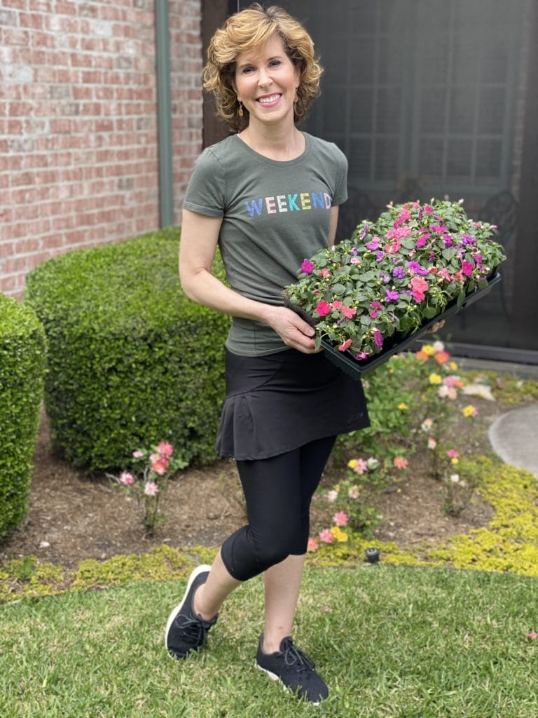 woman wearing graphic tee saying weekend and carrying flowers to plant