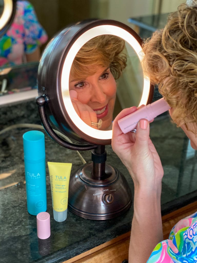 woman applying clean beauty product from pink tube to undereye area