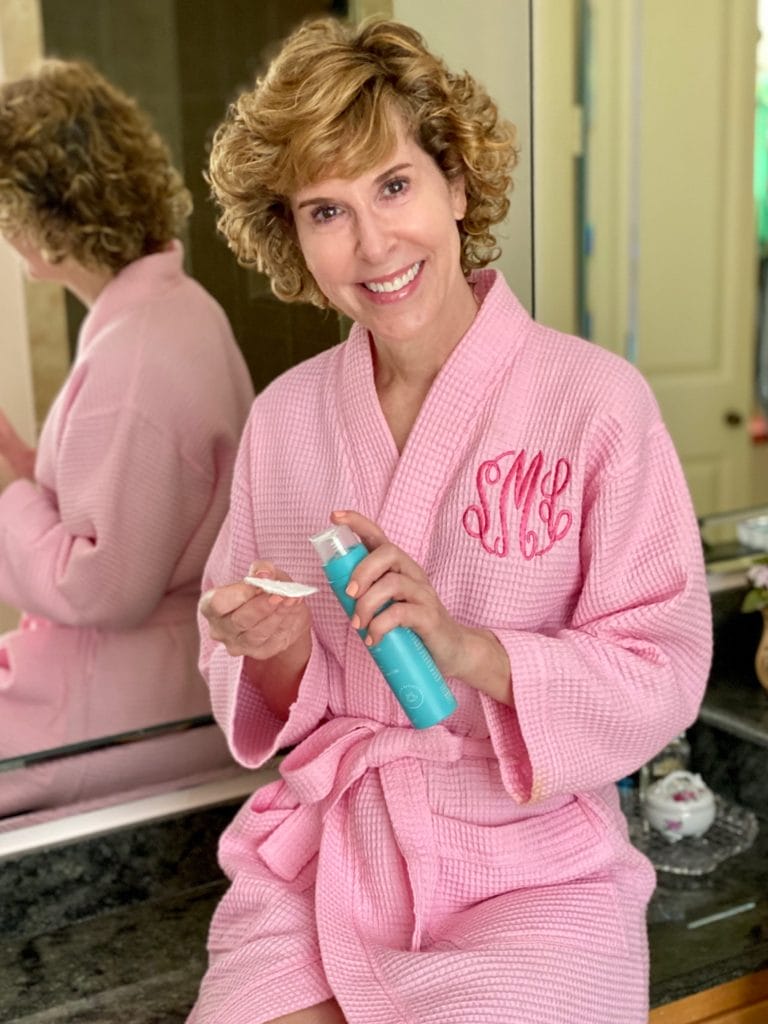 woman dressed in pink robe dispensing tula pro-glycolic 10% resurfacing toner on a cotton pad