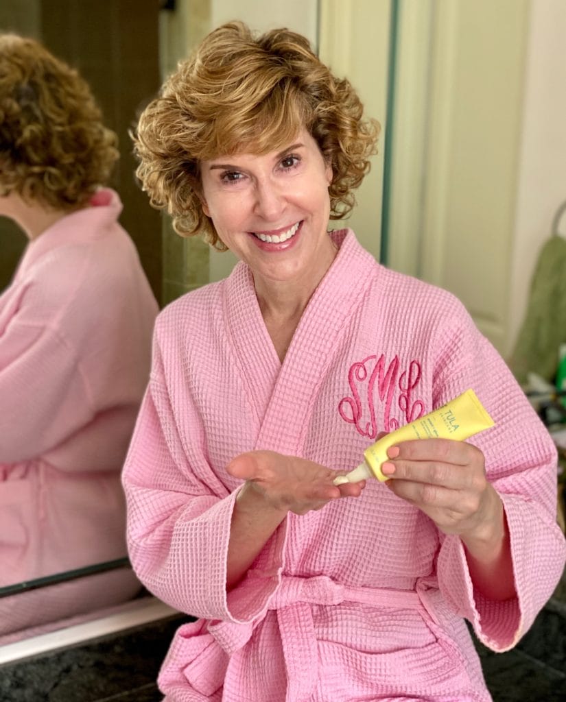 woman dressed in pink robe dispensing tula protect and glow sunscreen