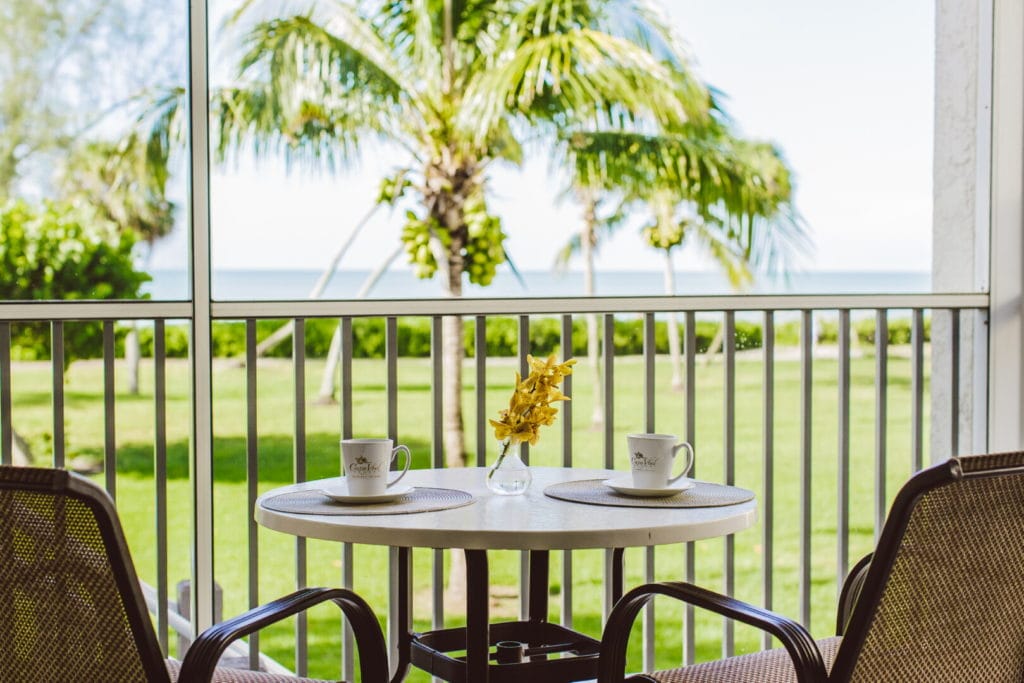 lanai of beach condo looking out at table and chairs and palm tree and beach