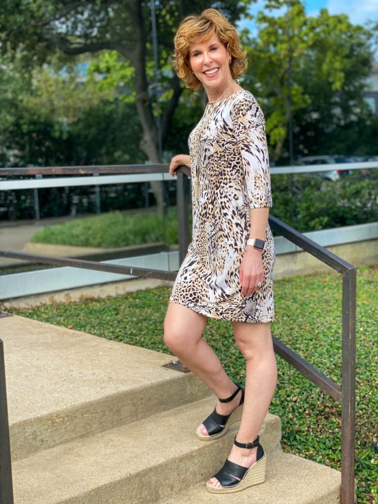 woman in animal print dress leaning against a stair railing in front of an office building