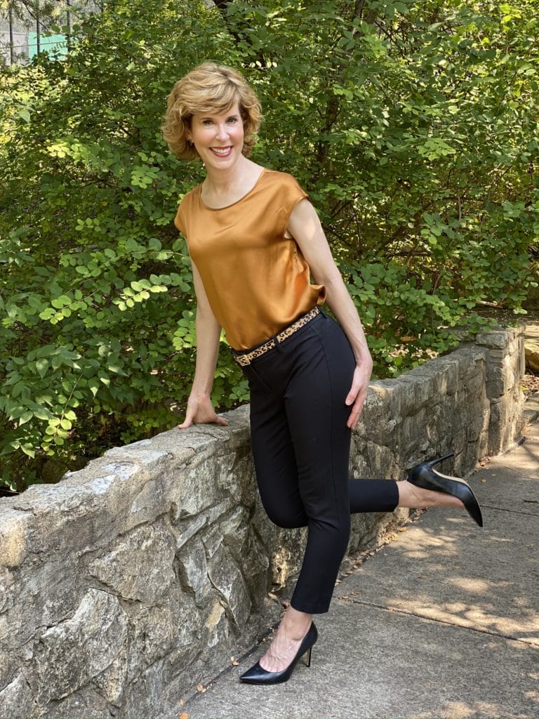 woman wearing lilysilk basic silk tee blak ankle pants leopard print belt black pumps standing on a stone bridge