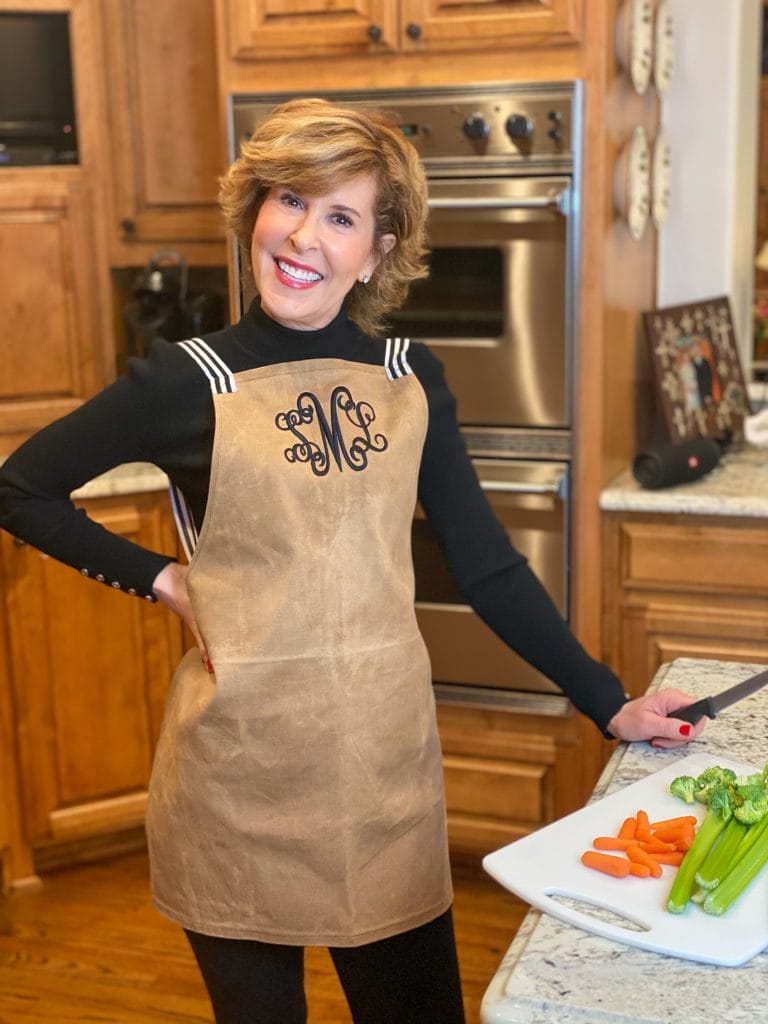 woman over 50 standing in kitchen wearing brown and black marley lilly monogrammed apron