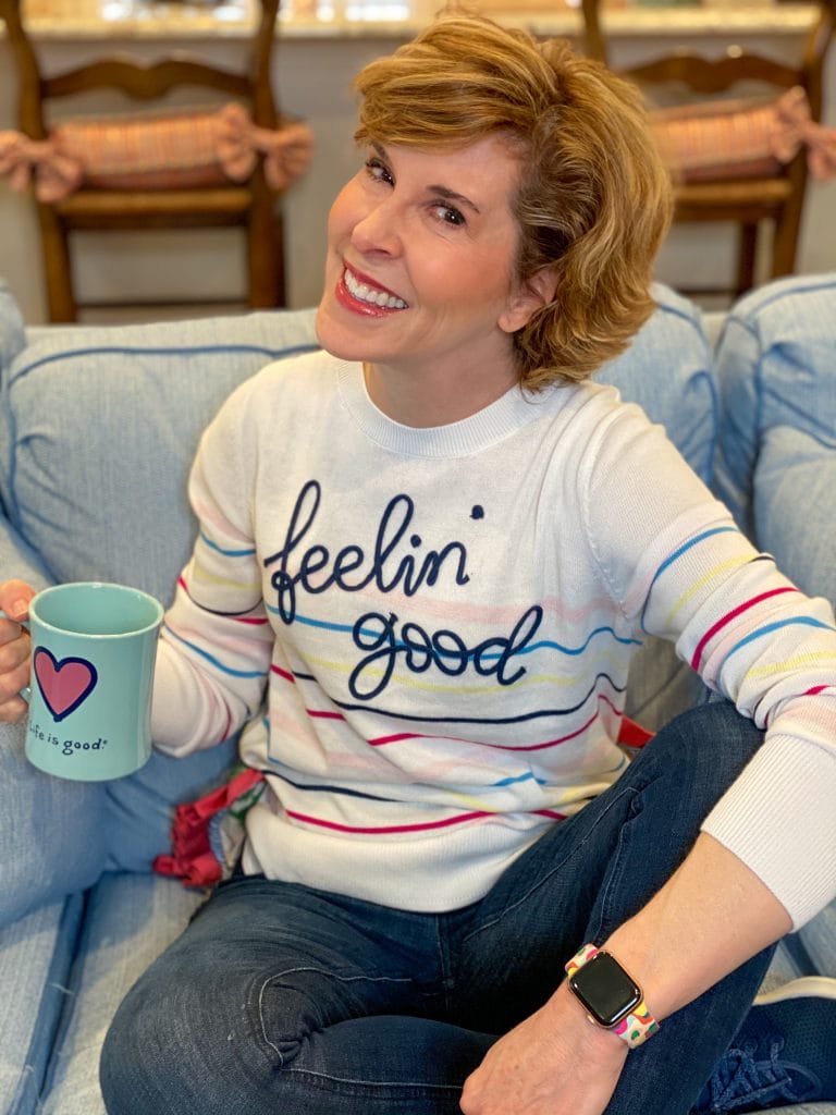 woman wearing walmart feelin' good striped sweater sitting on a sofa holidng a coffee cup talking about skin care over 50