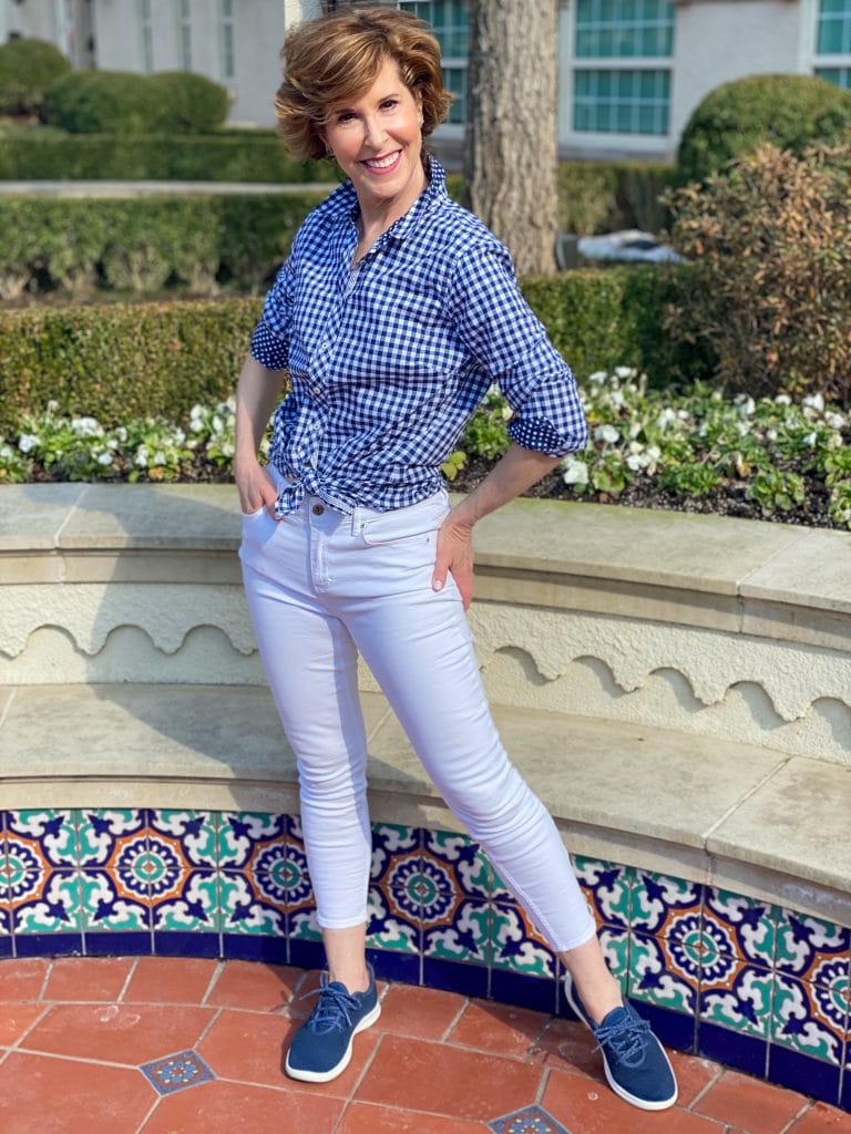 woman wearing talbots blue and white gingham shirt and white jeans with navy allbirds tree runner sneakers standing in front of a colorful low wall