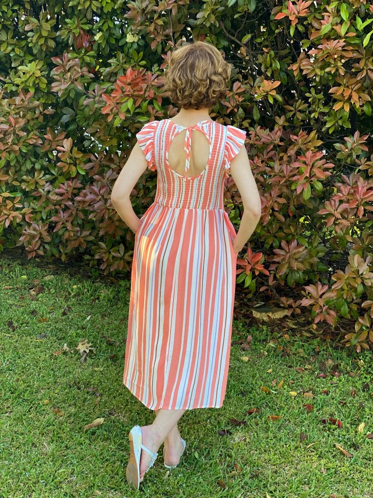 the back view of a woman over fifty wearing target's a new day Sleeveless Smocked nap Dress standing in front of a nandina bush
