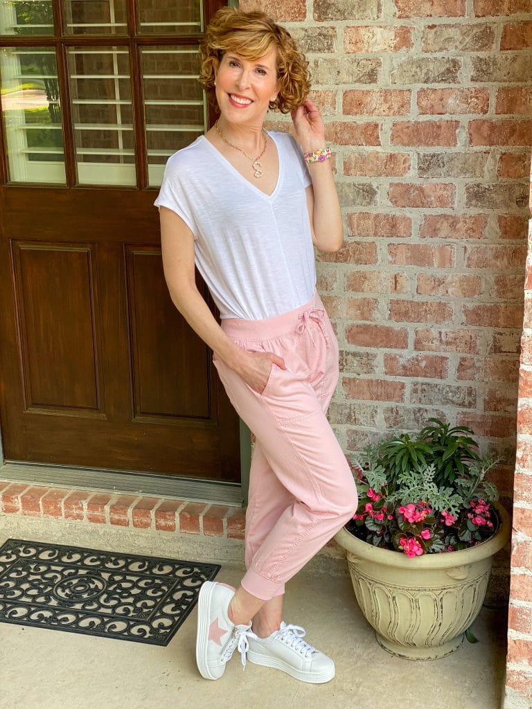 woman over 50 wearing pink twill joggers and a white WHBM jetsetter tee with a colorful apple watch band and sole bliss pink heart sneakers