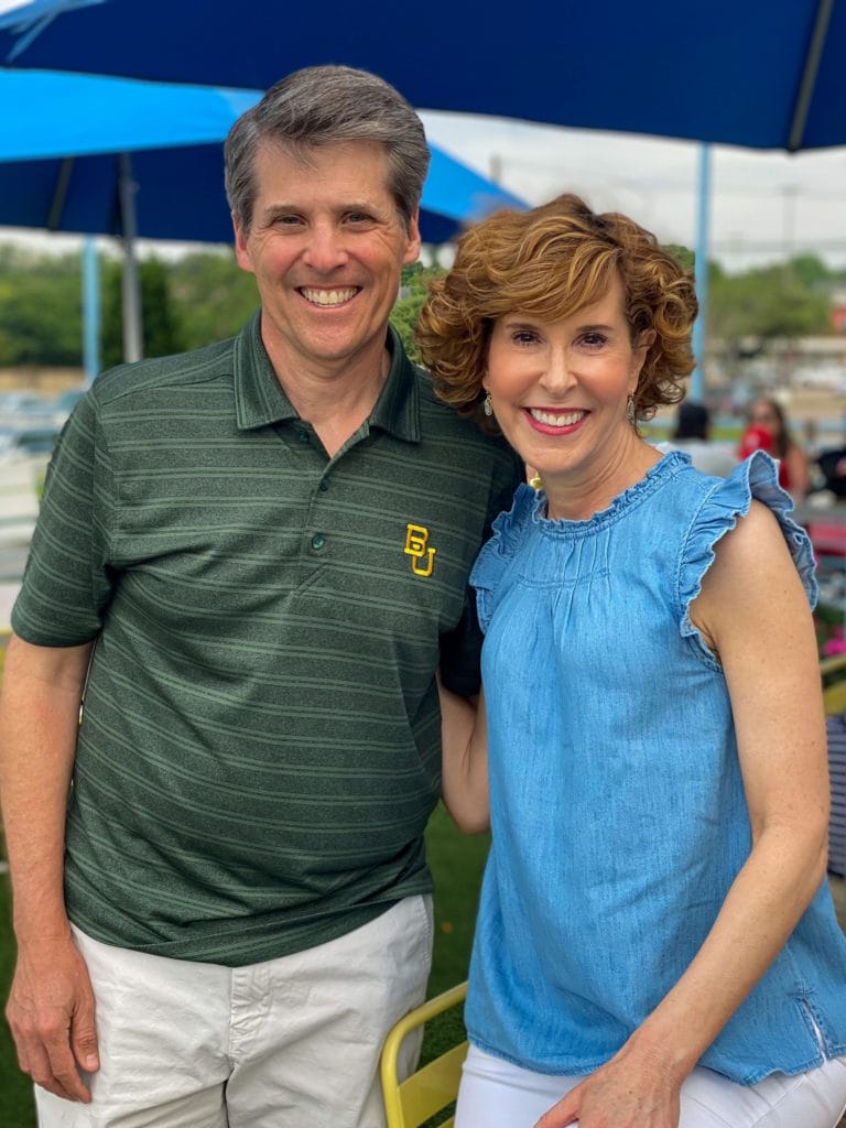 woman wearing chambray old navy ruffle sleeve and ruffle neck sleeveless top and husband wearing baylor university polo shirt standing on a restaurant patio