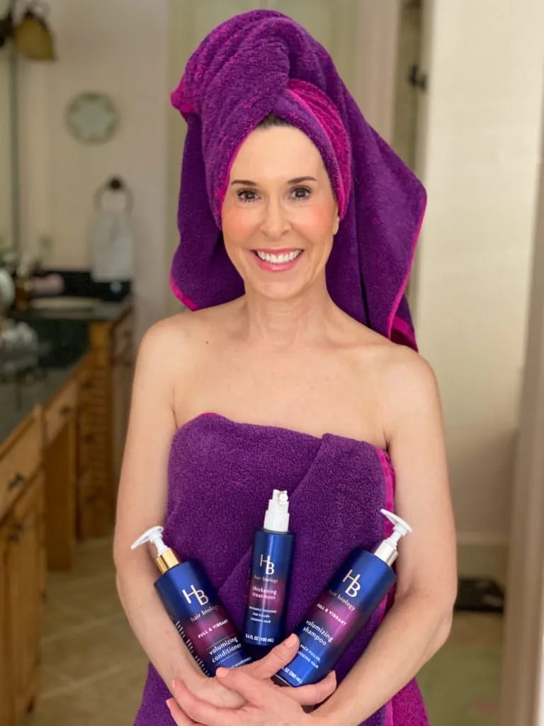 woman wrapped in purple towel holding hair biology products