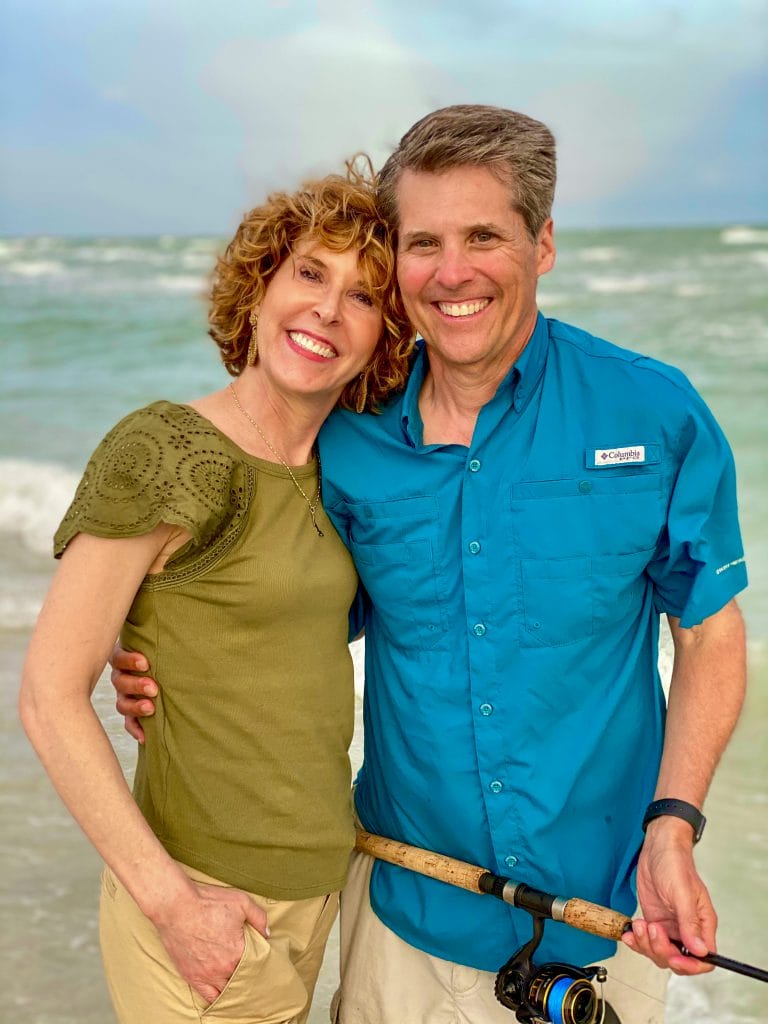 middle age couple on beach man wearing teal fishing shirt woman wearing sage green eyelet flutter sleeve shirt