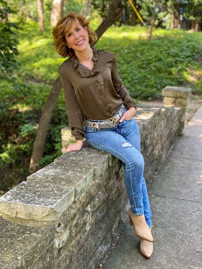 woman wearing cabi icon blouse, cinch skinny, and serpent belt with vince camuto taupe suede booties sitting on the side of a bridge