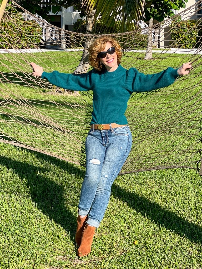 woman wearing jcrew Cashmere puff-sleeve mockneck sweater and jeans with brown booties standing up leaning against a hammock