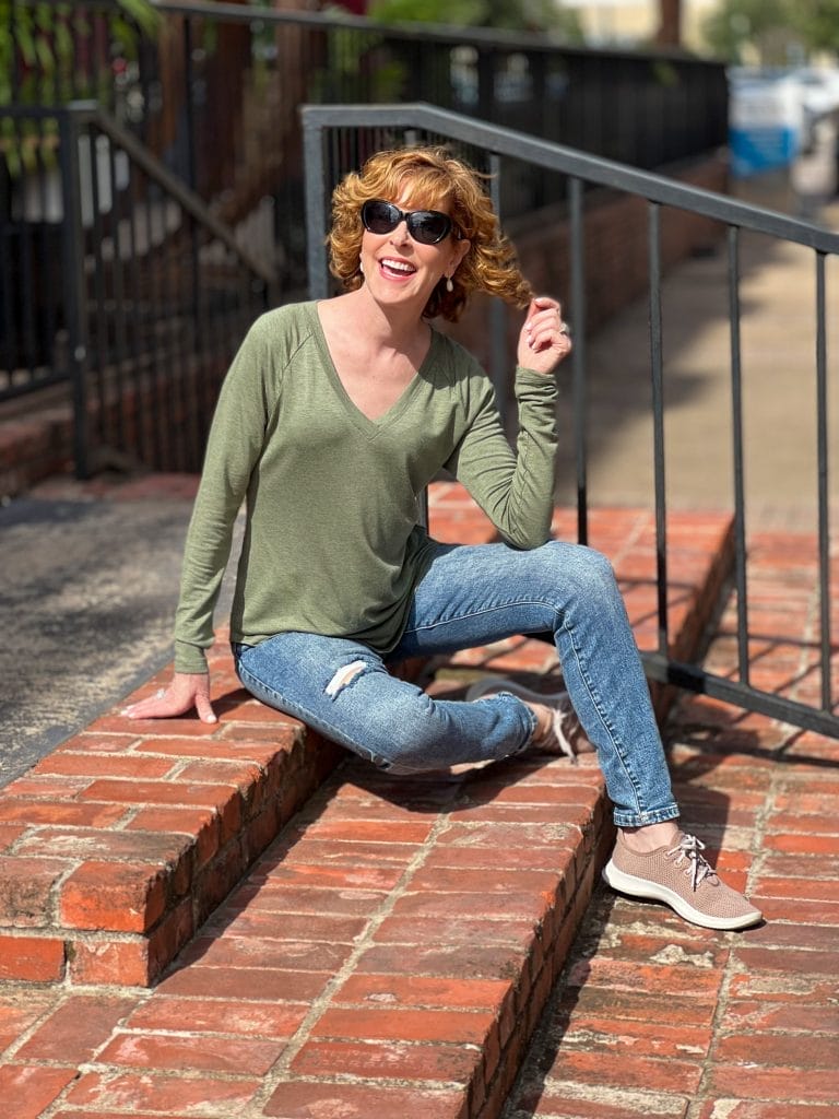 woman over 50 wearing cabi recline tee and cinch skinny jeans sittring on a brick staircase outside
