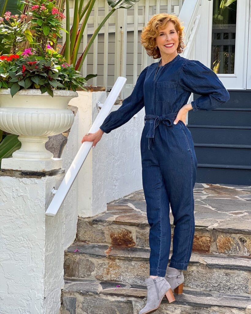 woman over 50 posing on a staircase wearing a denim jumpsuit