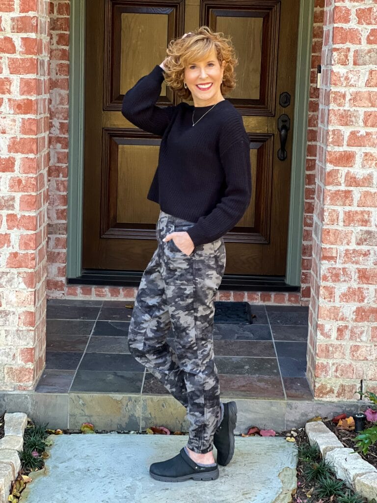 woman over 50 posing on her front porch wearing spanx camo joggers and jambu Haven mules with a black sweater