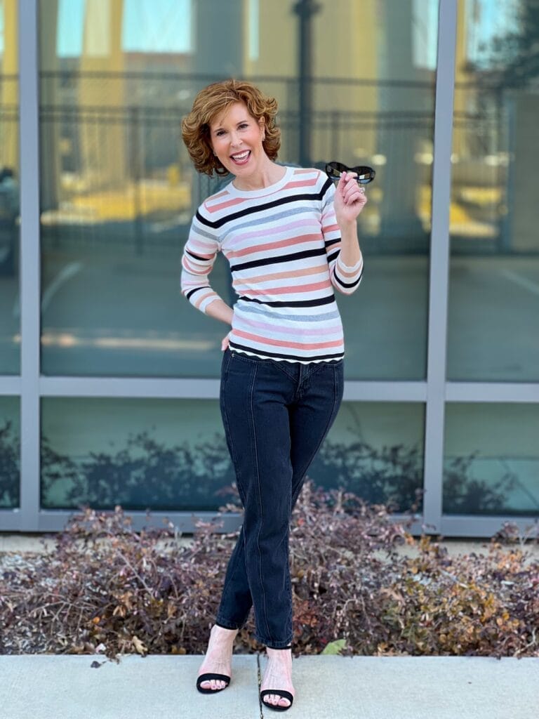 woman over 50 standing in front of a mirrored window wearing Halogen® Ribbed Crewneck Sweater and black seamed Mom jeans by Nordstrom showing how to transition your wardrobe from winter to spring with Nordstrom made brands