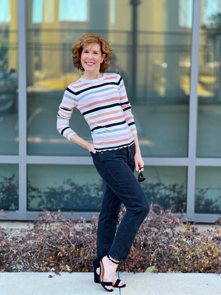 woman over 50 standing in front of a mirrored window wearing Halogen® Ribbed Crewneck Sweater and black seamed  Mom jeans by Nordstrom showing how to transition your wardrobe from winter to spring with Nordstrom made brands