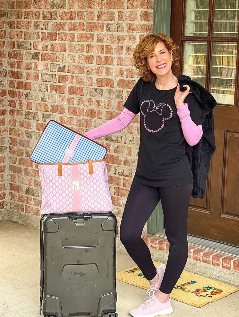 woman wearing pink sparkly minnie mouse outline black tee standing with suitcase about to go on a multi-generational disney trip